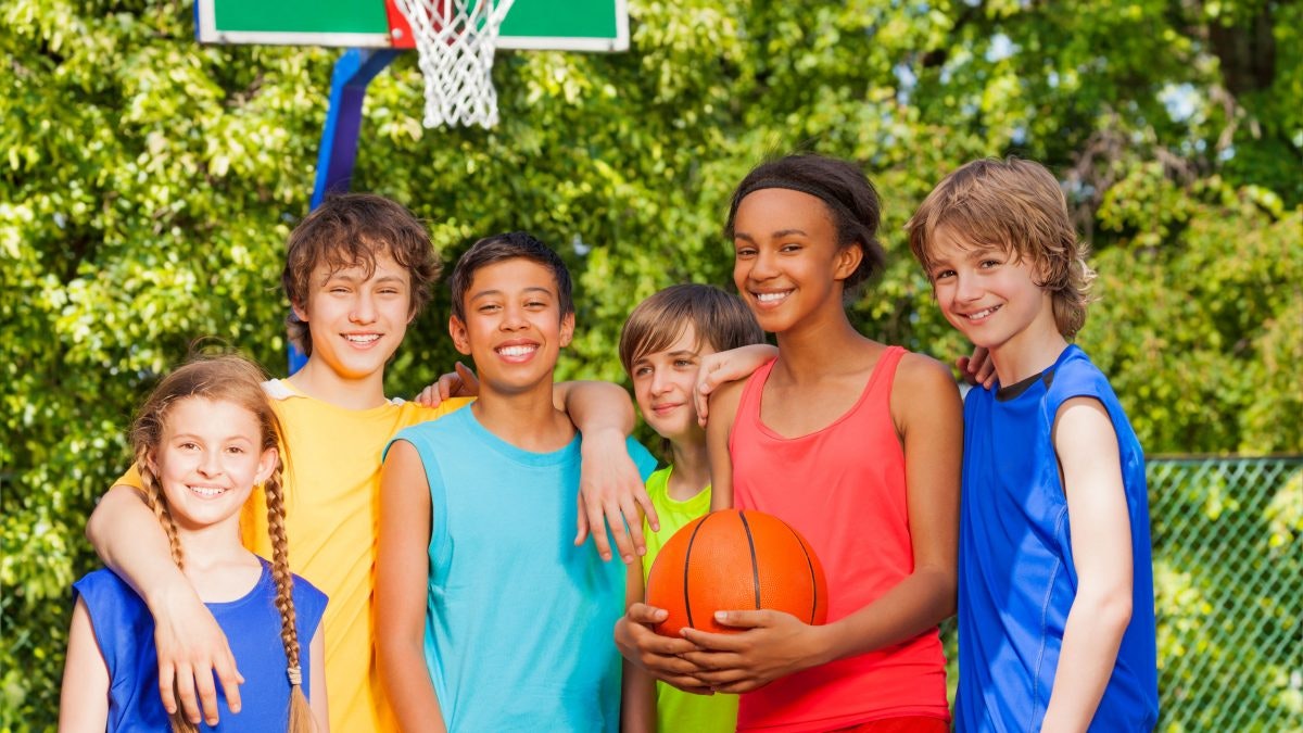 A group of happy children with a basketball posing in front of a hoop.