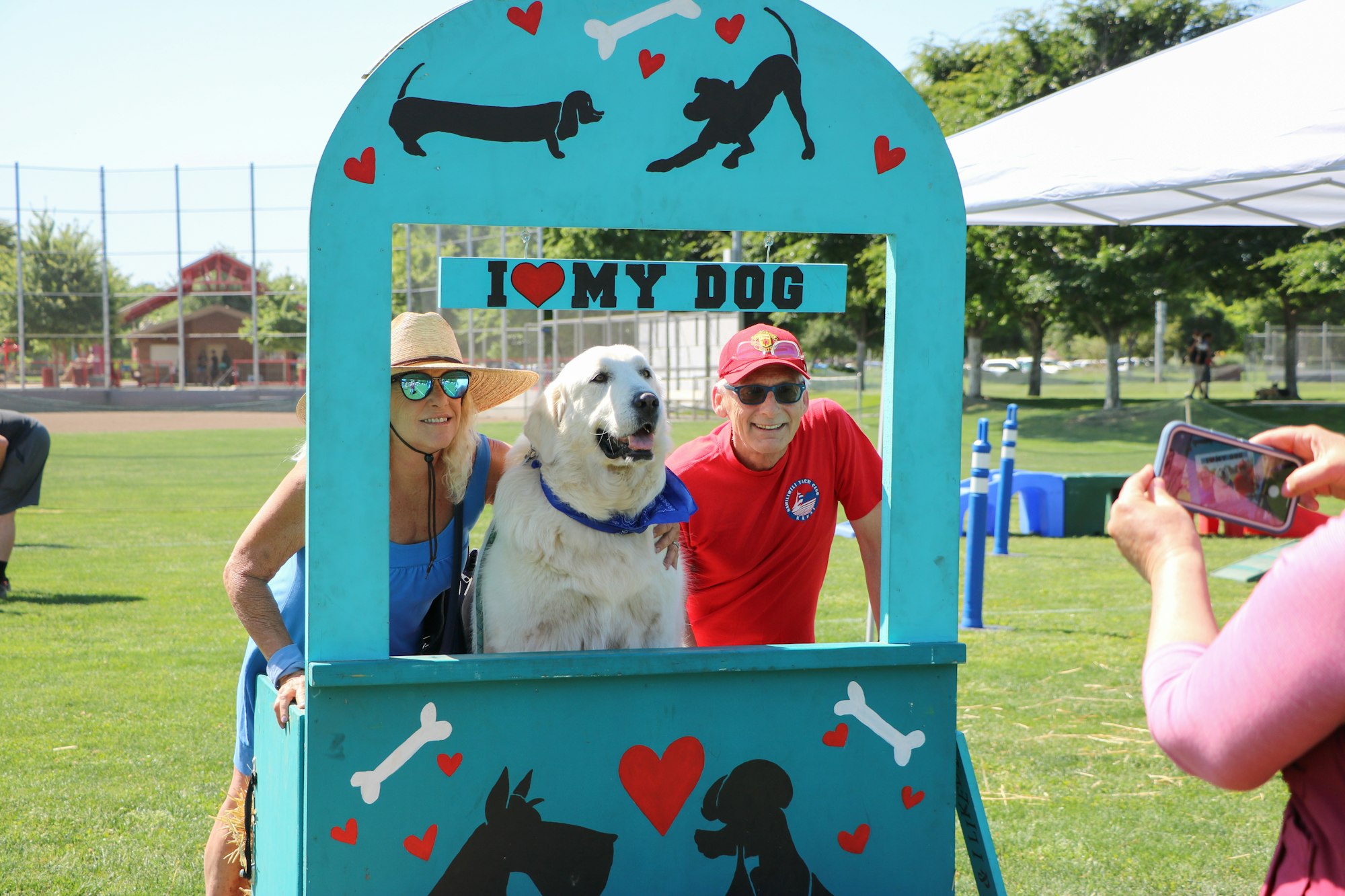 Two people and a dog posing in a cutout frame with the text "I love my dog" while another person takes their photo.