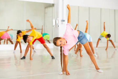Children in a dance class doing a stretching exercise, wearing colorful outfits.