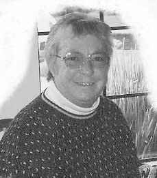 A person wearing glasses and a patterned sweater is smiling indoors near a window.