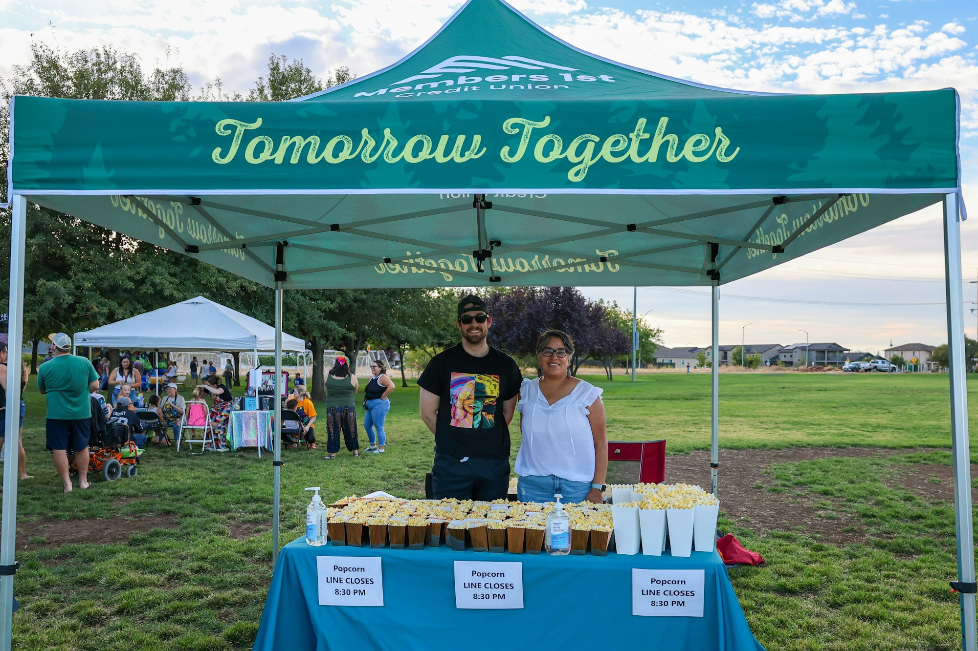 Two people at a popcorn stand under a tent marked "Tomorrow Together" at an outdoor event.