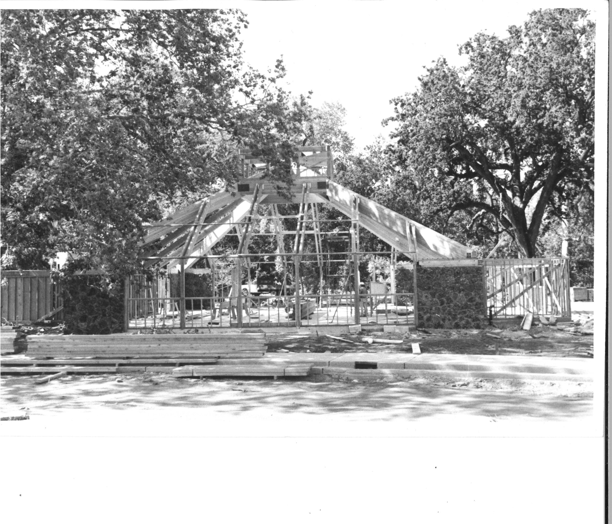 A wooden construction frame among trees, possibly for a house or structure, with scattered building materials on the ground.