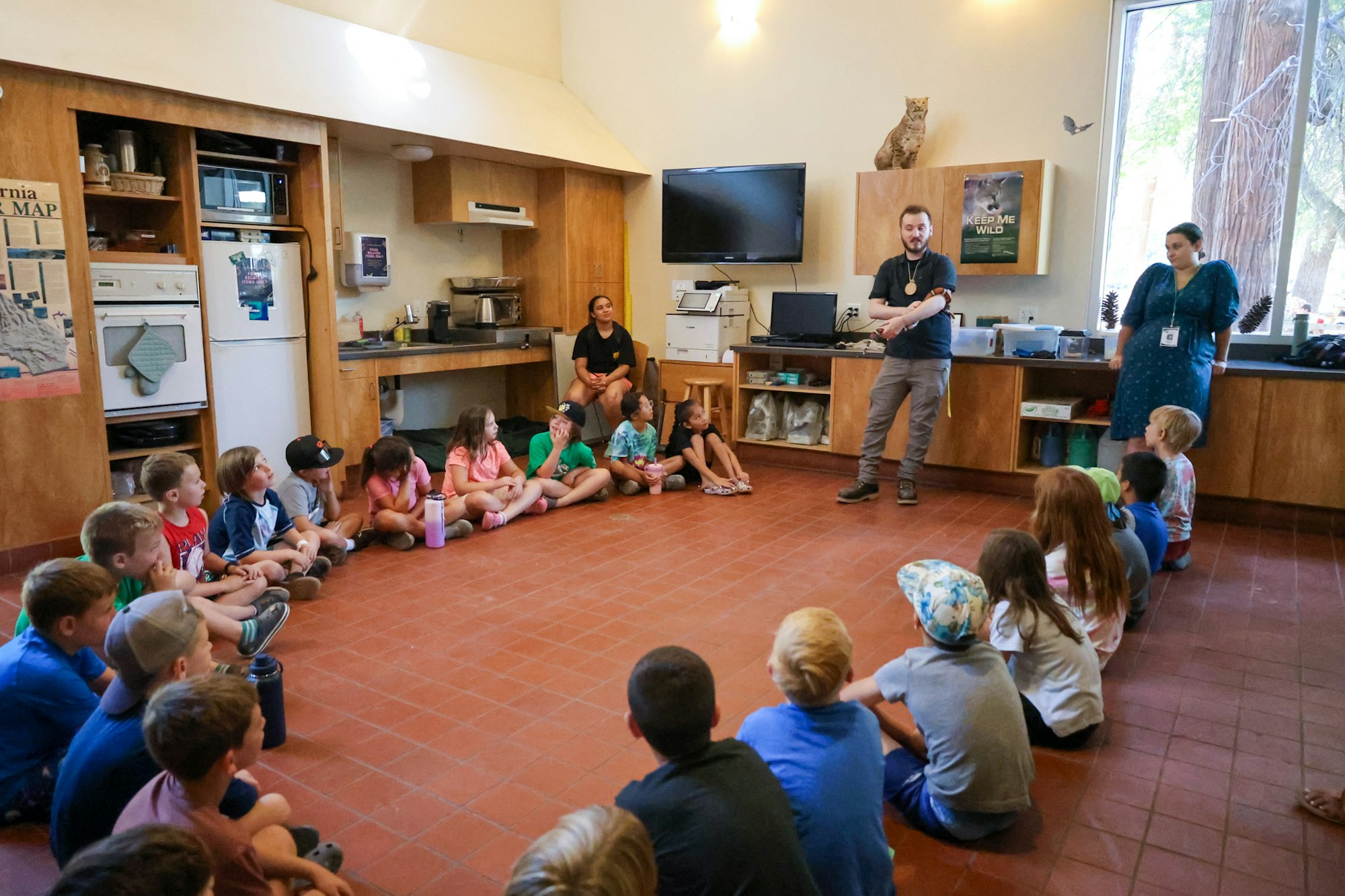 Children sitting on the floor listening to a presenter in a room with wildlife exhibits.