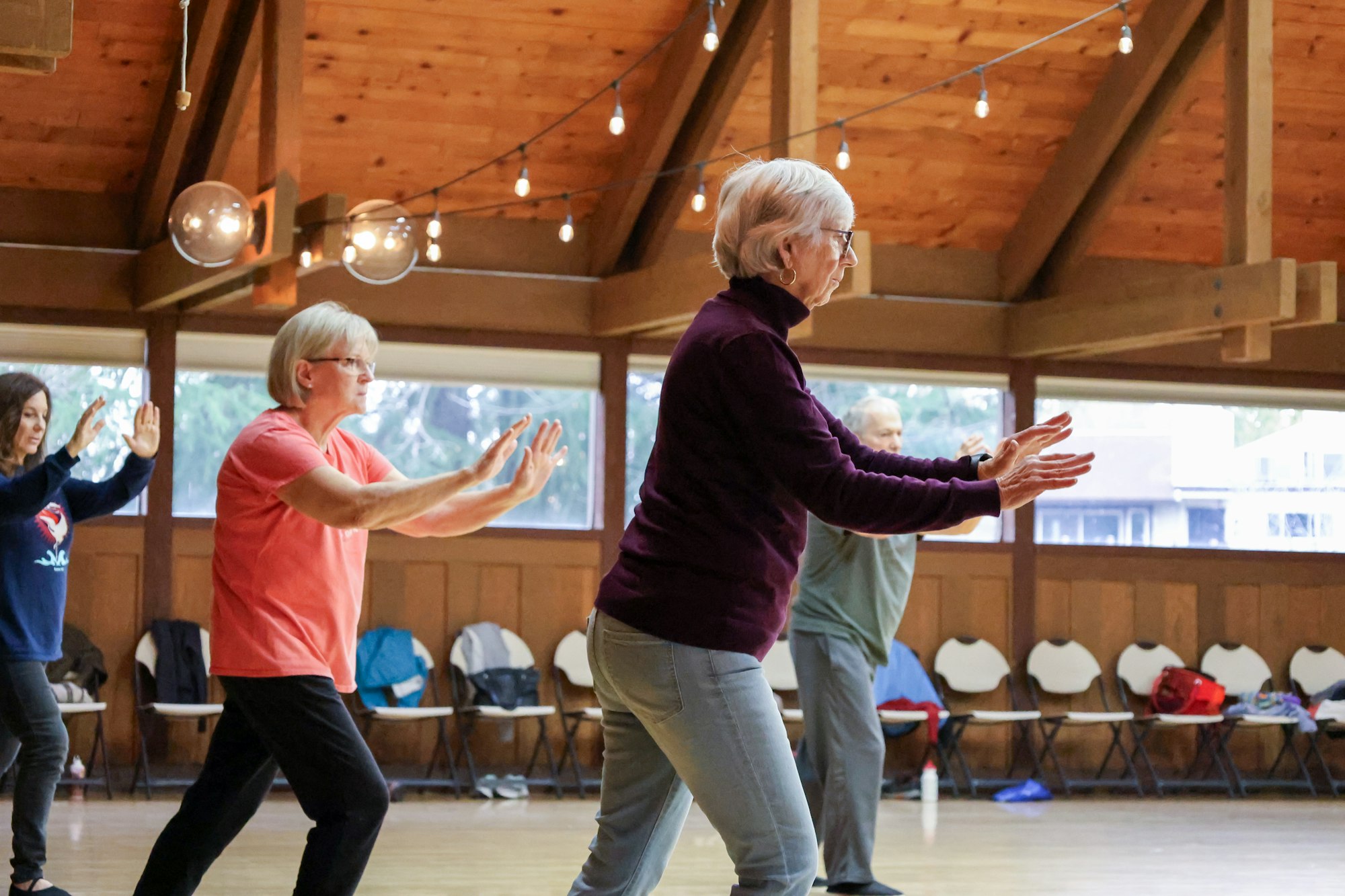 People practicing tai chi in a hall with wooden interiors.