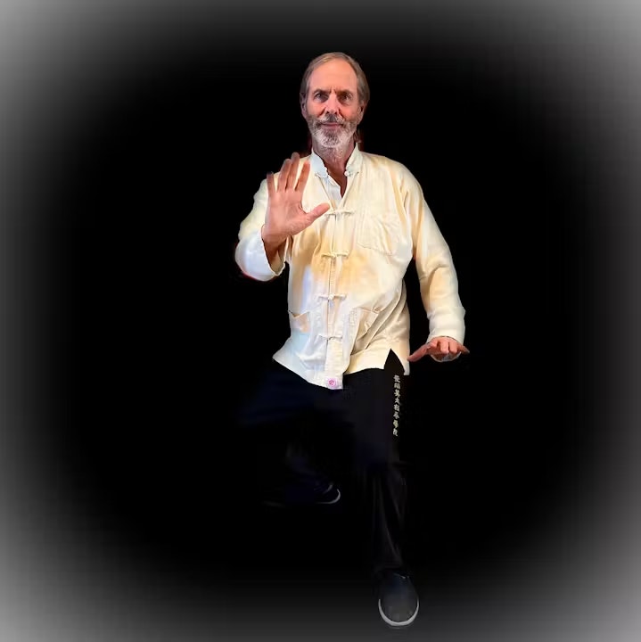 A man in traditional martial arts attire poses in a dynamic stance against a black background.