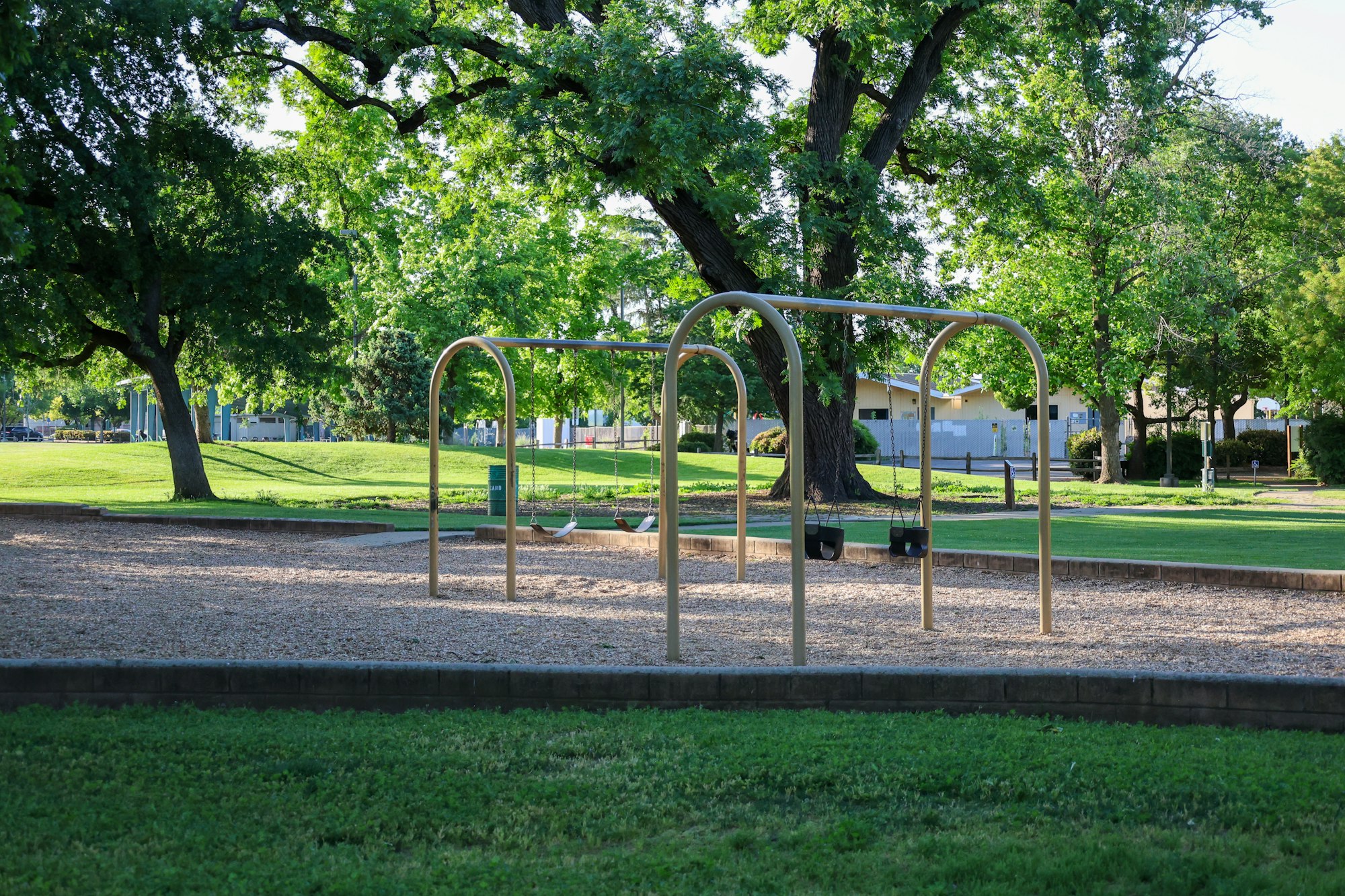 A tranquil park with swing set, green trees, and grass.