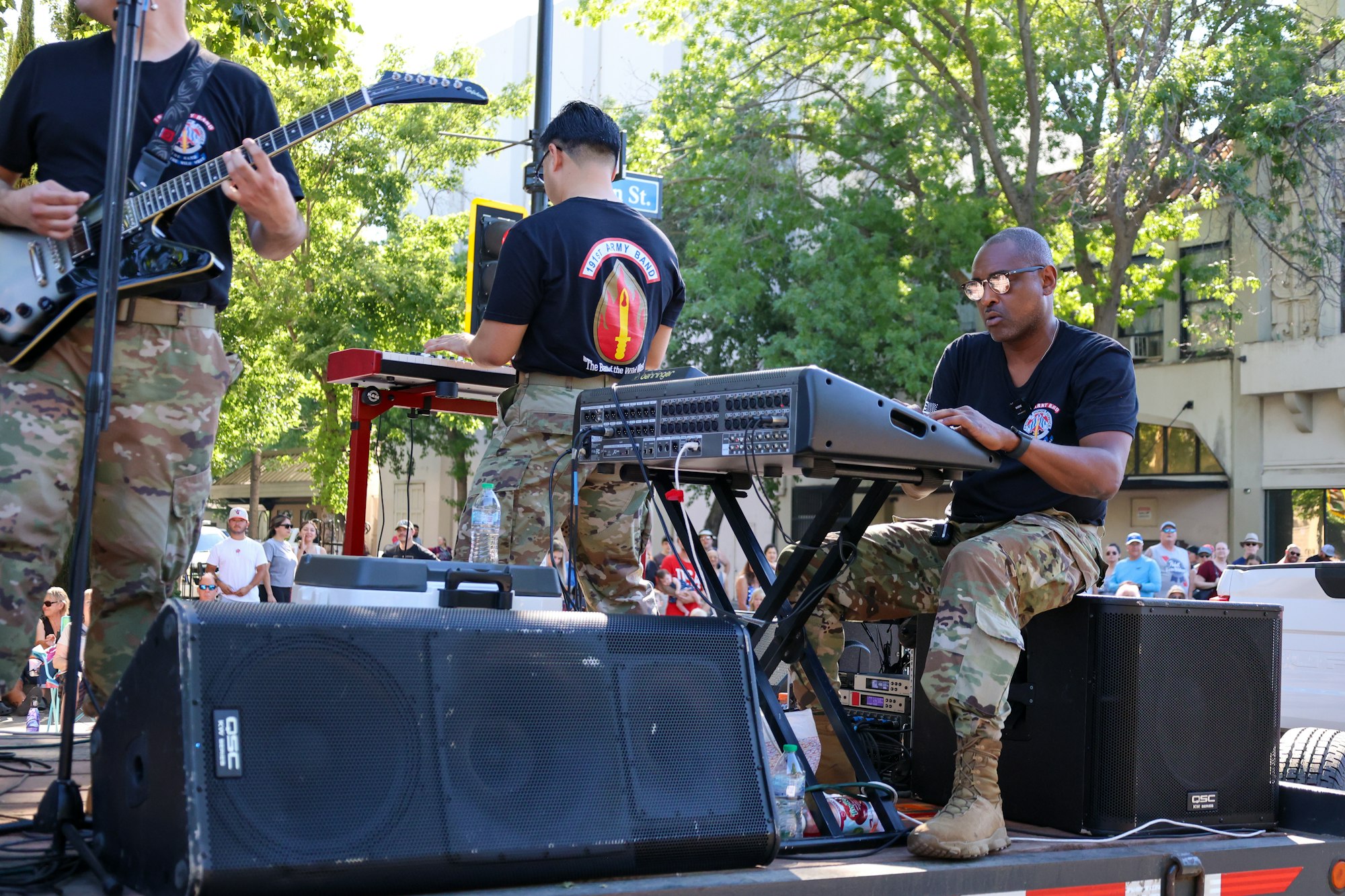 A group of musicians in military uniform performing outdoors with guitars and keyboards.