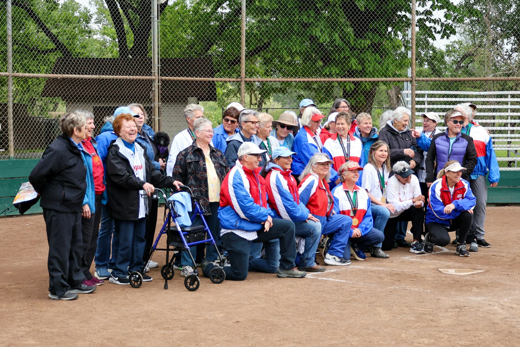 A group of older adults in sportswear posing on a baseball field.