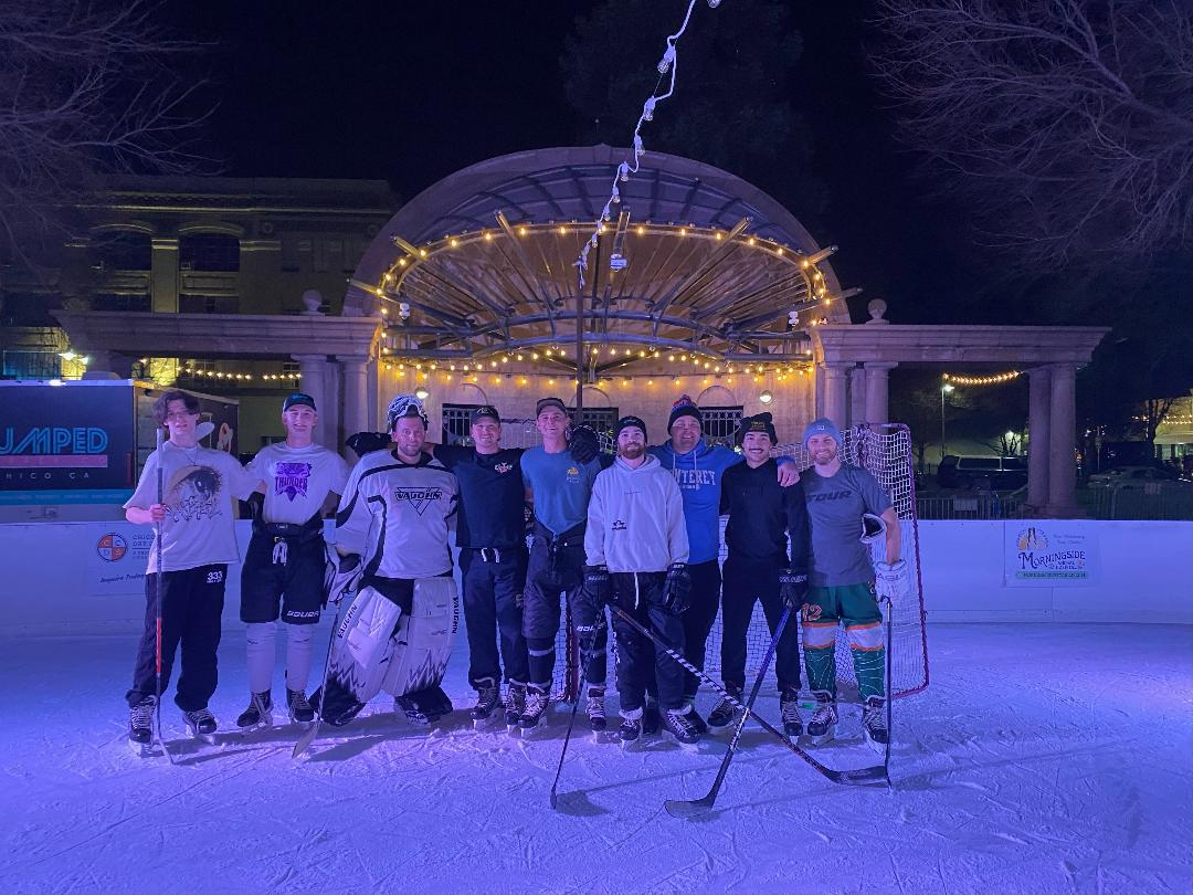 A group of people with hockey gear standing on an ice rink at night, with lights and an archway in the background.