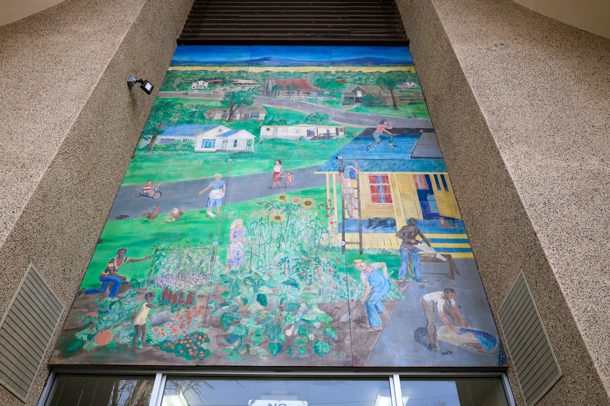 A colorful mural depicting a rural community scene with people gardening, working, and interacting near houses.