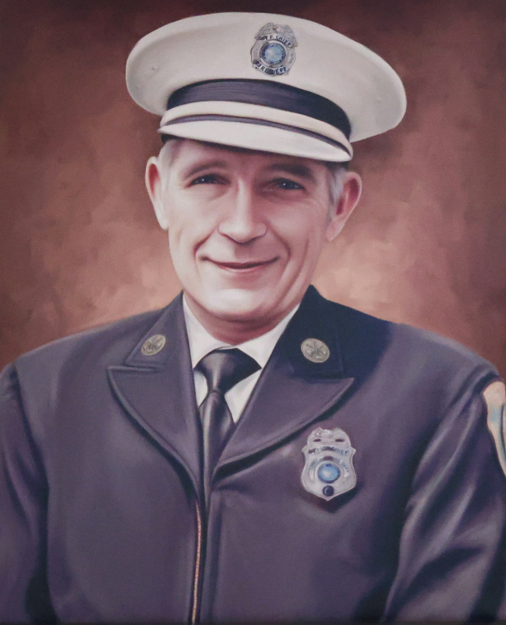 A person wearing a fire department uniform with a badge and hat, smiling.