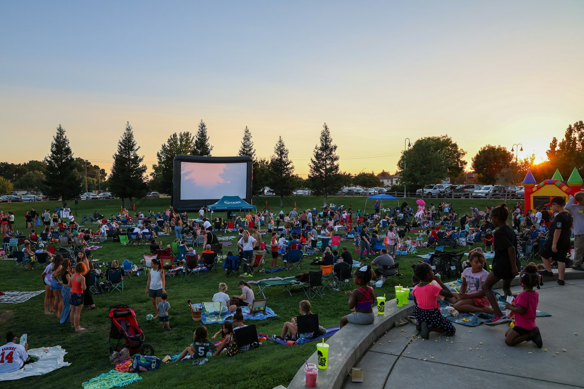 Outdoor movie event in a park with a large crowd sitting on the grass.