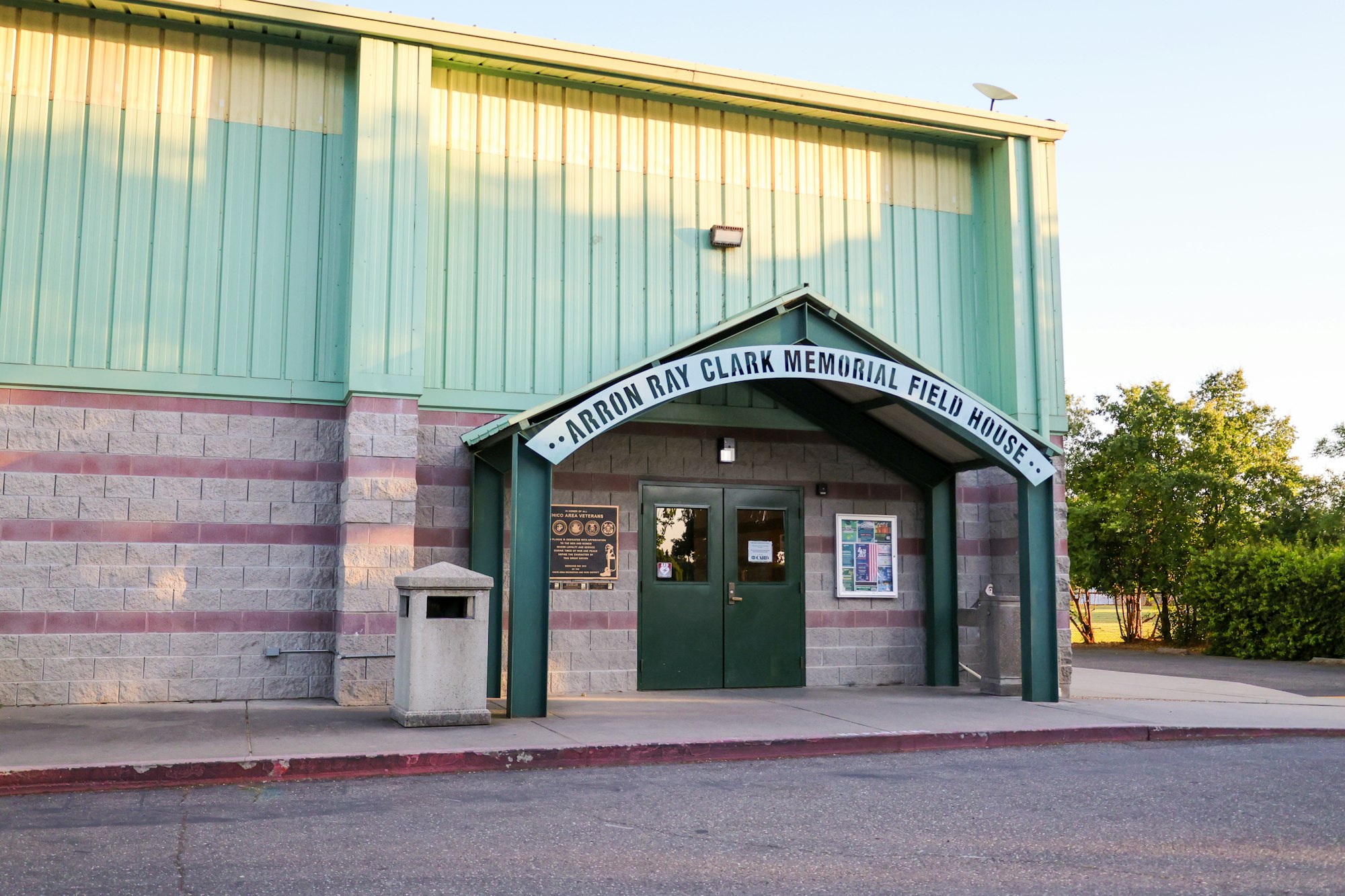 Entrance of the "Arron Ray Clark Memorial Field House" with green doors and a trash can nearby.