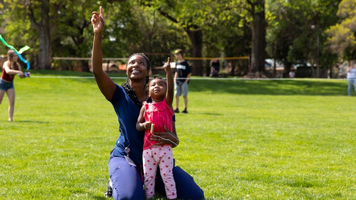 A mother and daughter point up to the sky enjoying Kite Day!