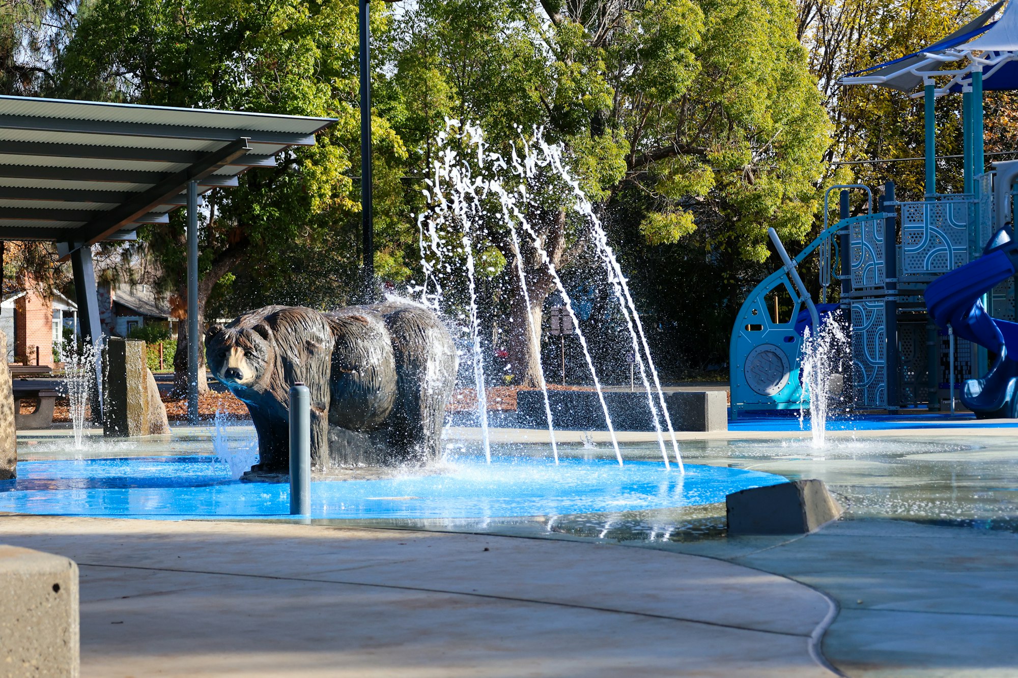 A playground with water features and a bear statue.