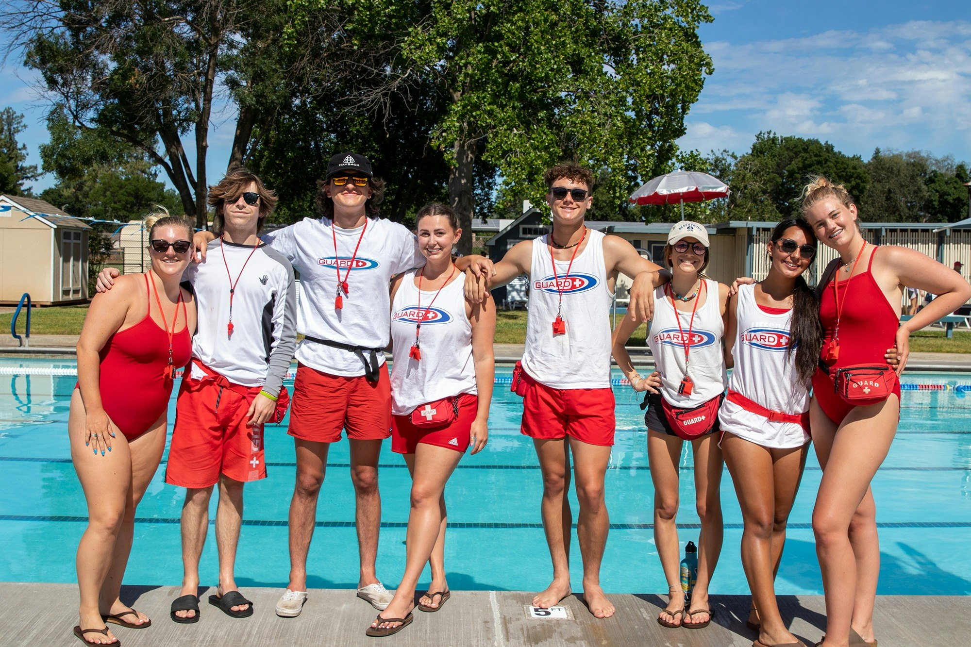 A group of CARD lifeguards stand together in front of a pool and smile for a photo.
