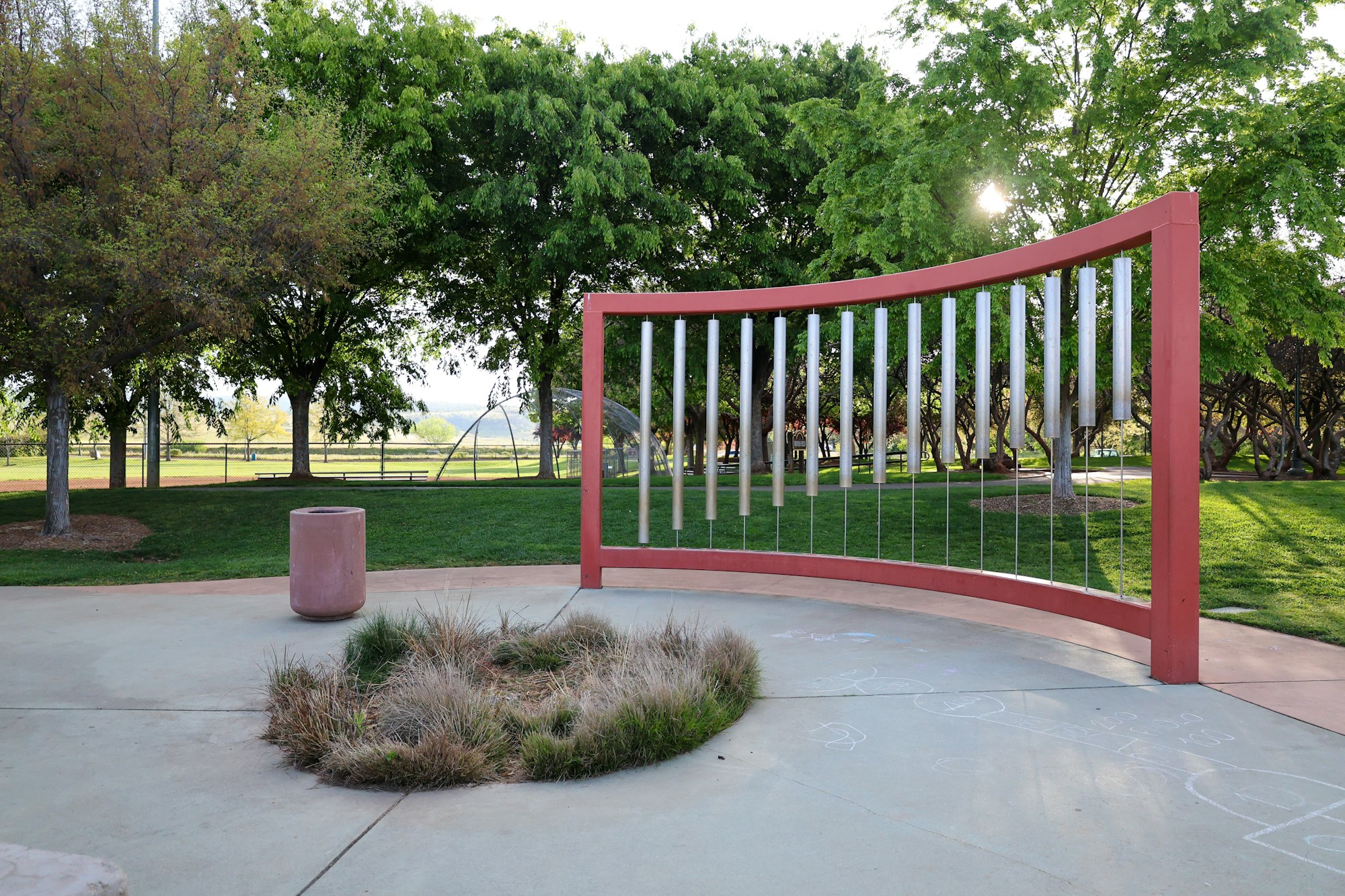 A large outdoor xylophone, trees, grass, and sidewalk in a park.