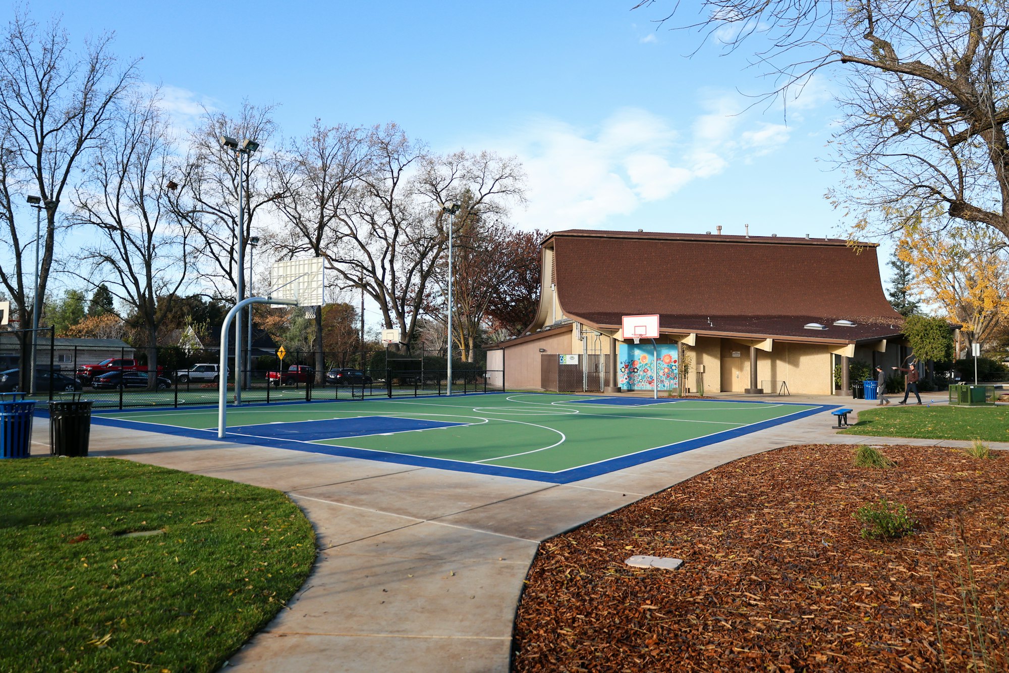 A colorful outdoor basketball court, a building with murals, trees, and a clear sky.