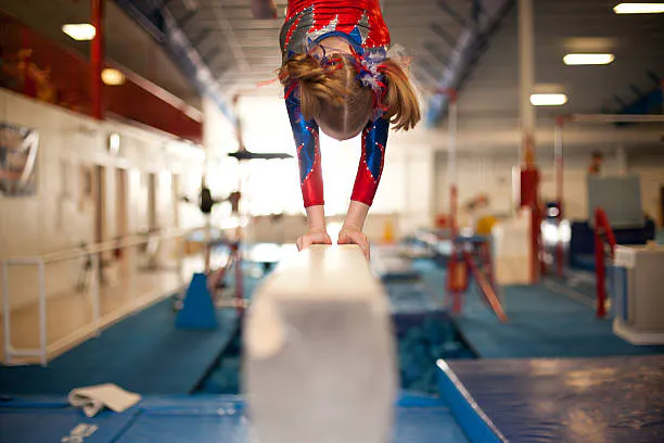 Gymnast performing on balance beam in a gym.