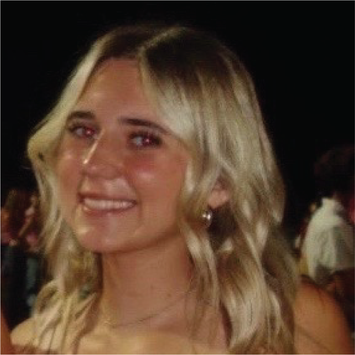 A person with long, wavy blonde hair smiling in a dimly lit setting.