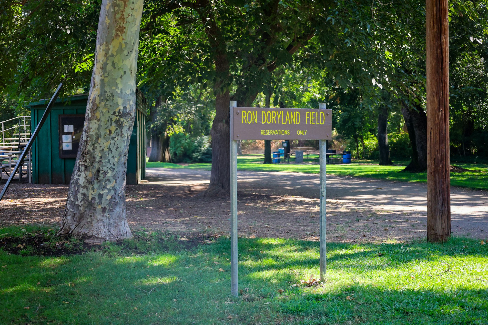 Sign reading "Ron Doryland Field Reservations Only" in a park setting with trees and a path.