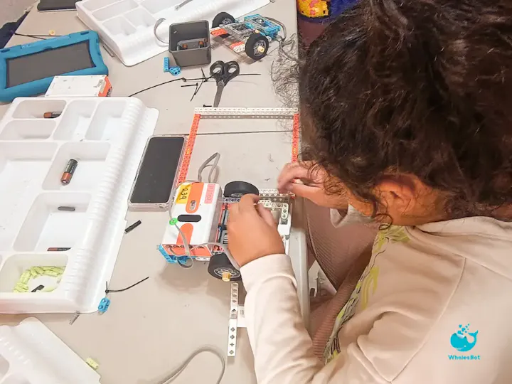 A child is assembling a robotic car using various parts on a table filled with tools and materials.