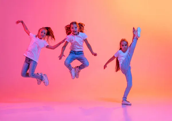 Three kids jumping against a pink and orange gradient background.