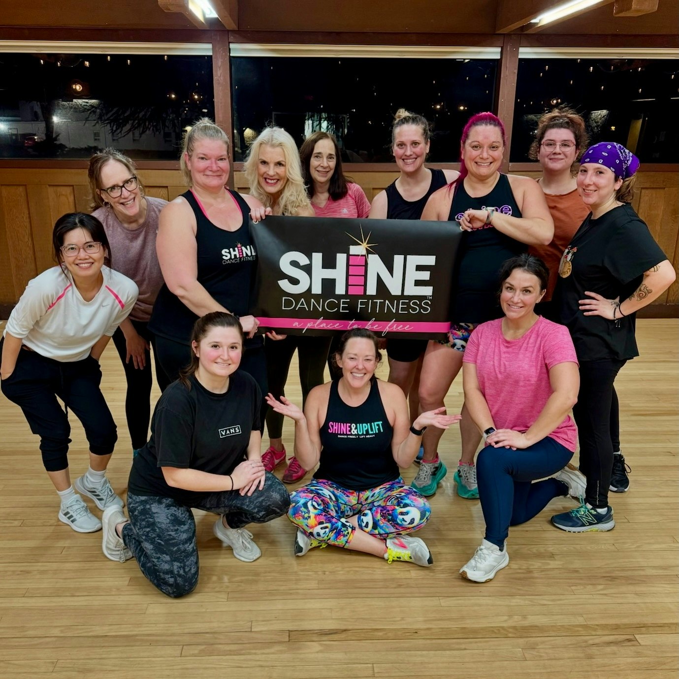 Group photo of people at a dance fitness class holding a "SHINE DANCE FITNESS" banner.