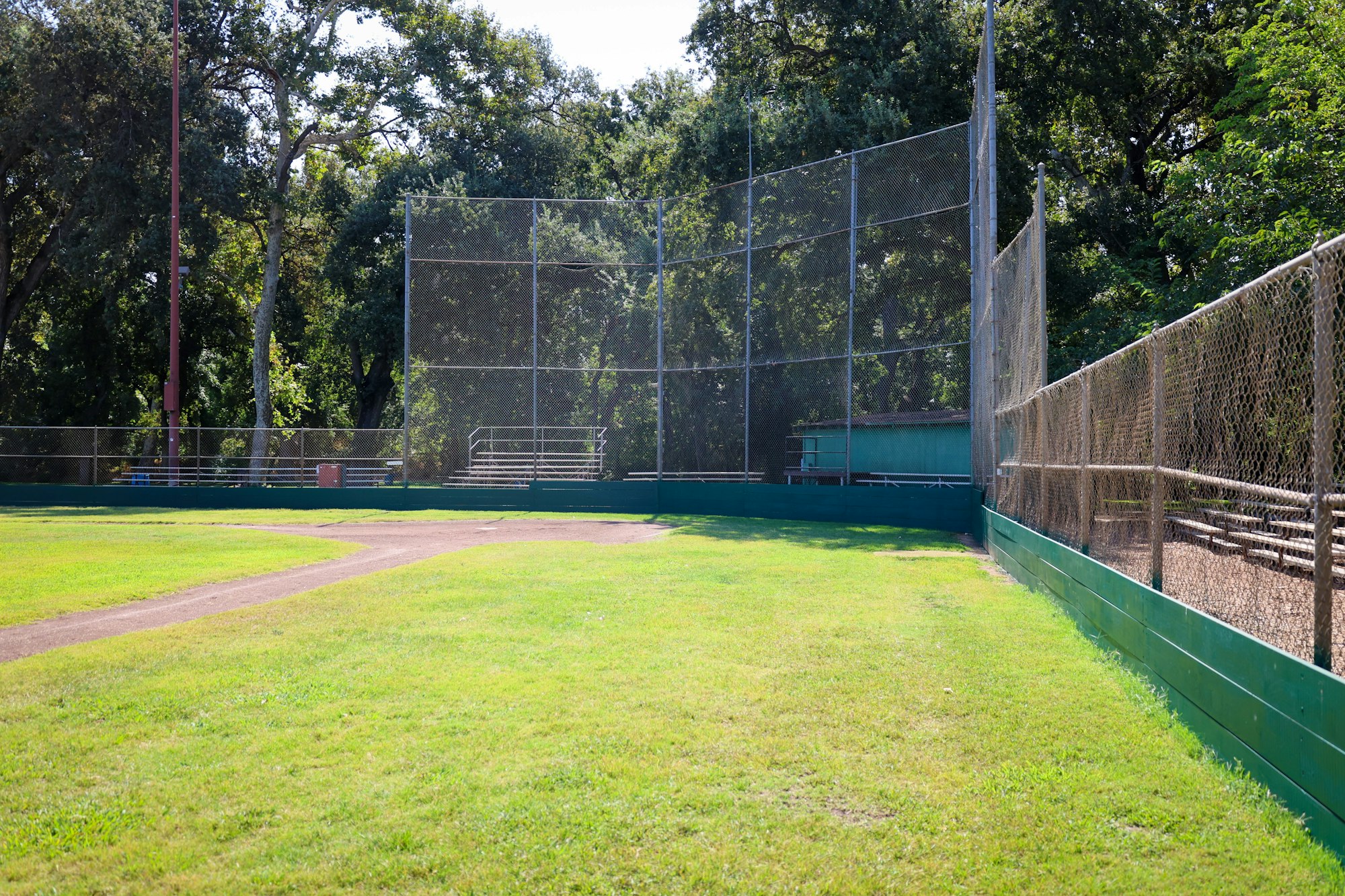A baseball field with a chain-link fence, green grass, and bleachers in the background.