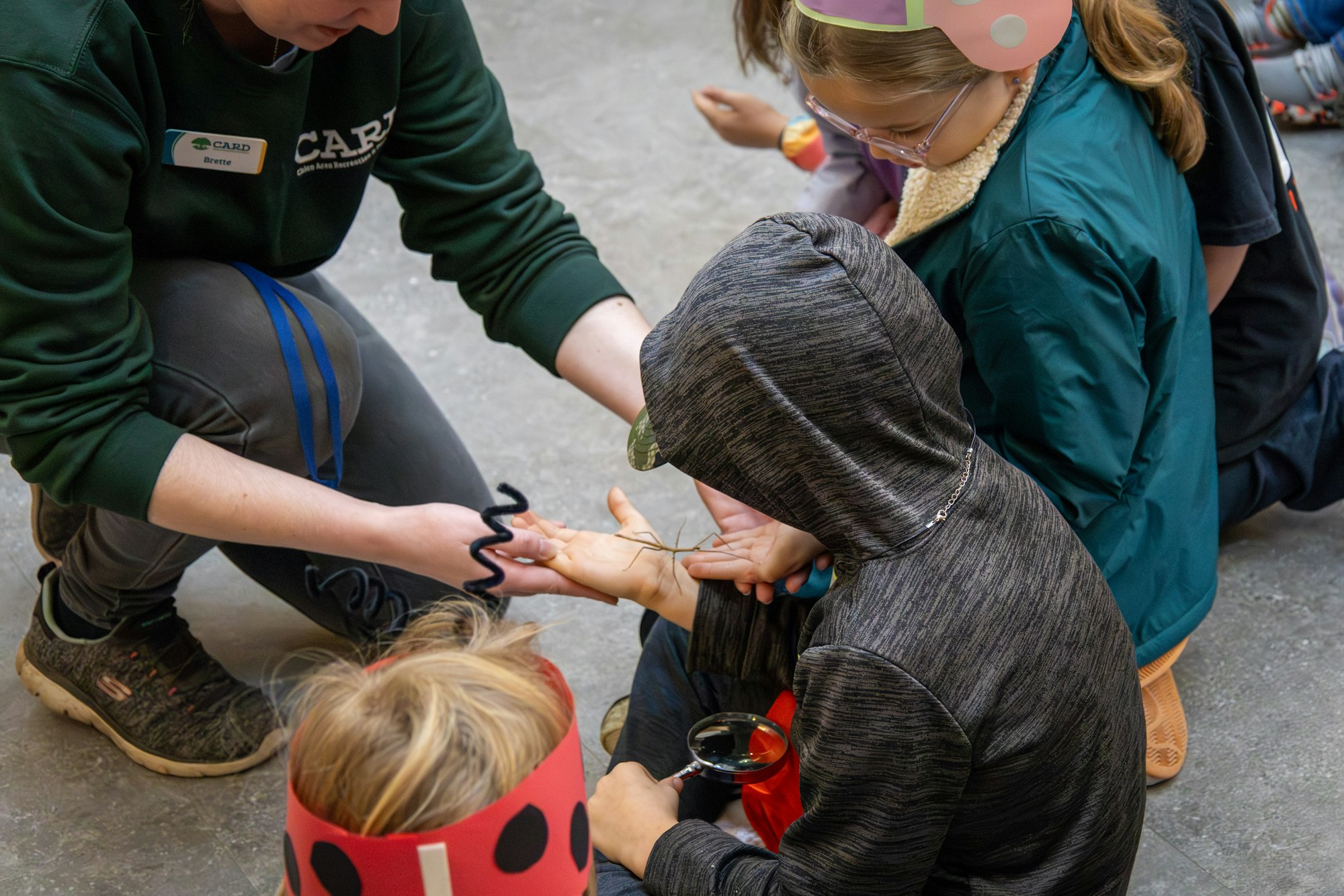 A person shows a child a creature on their hand while others observe, engaged in a hands-on learning activity.