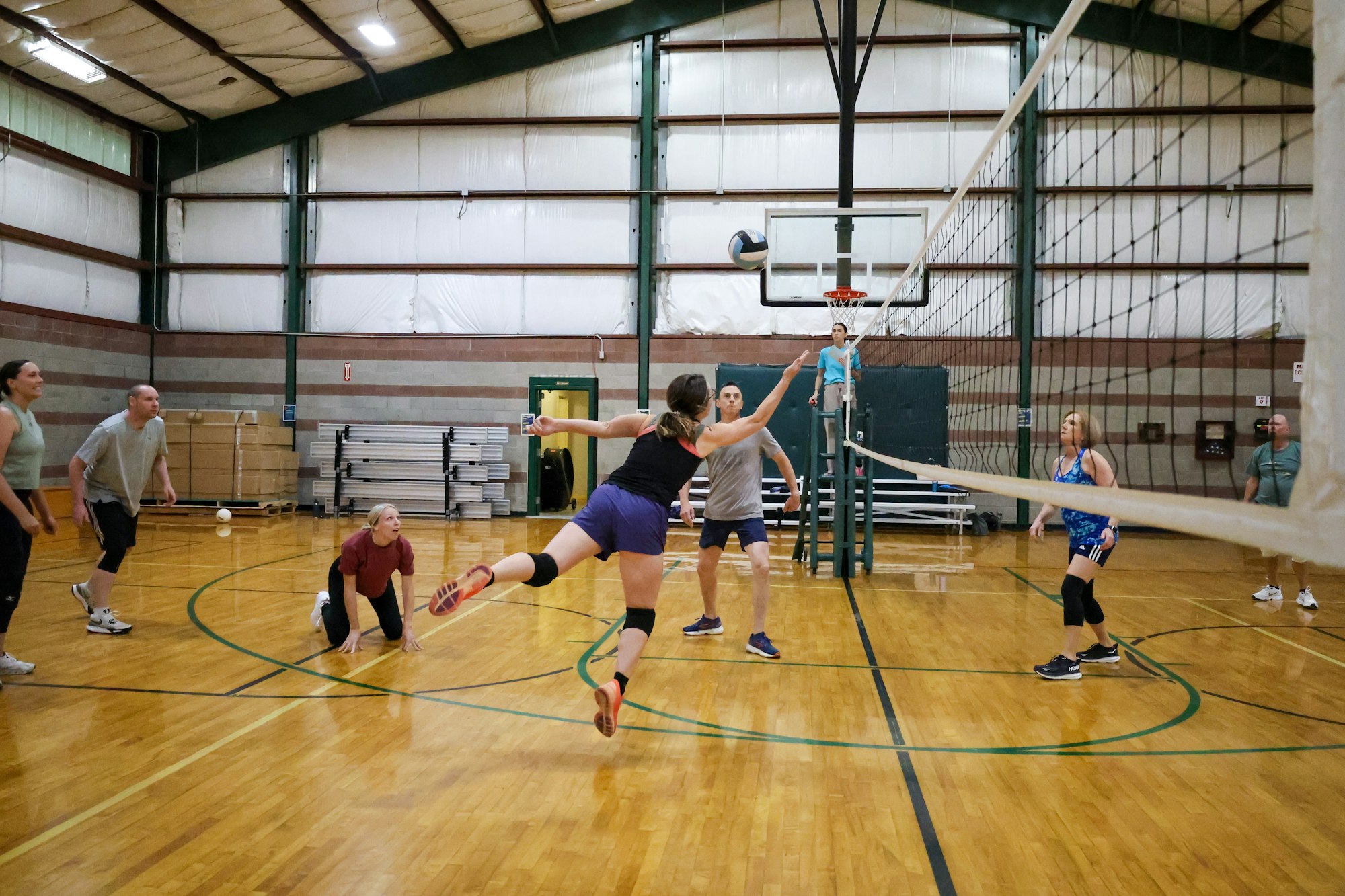People playing volleyball in an indoor gym, one player leaping to hit the ball.
