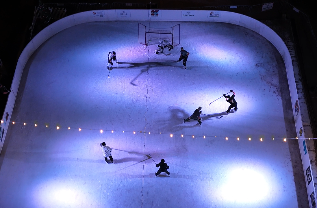 Aerial view of people playing hockey on an illuminated ice rink.