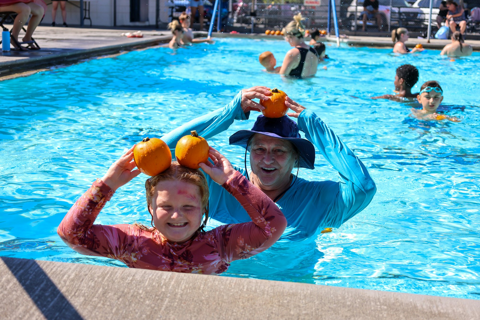 People in a pool holding pumpkins over their heads, enjoying a sunny day.