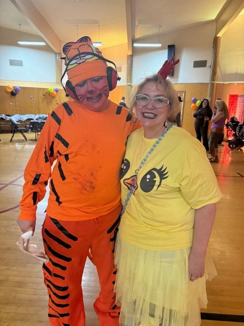 A woman in a yellow dress and a man in an orange tiger costume are posing together in a festive indoor setting.