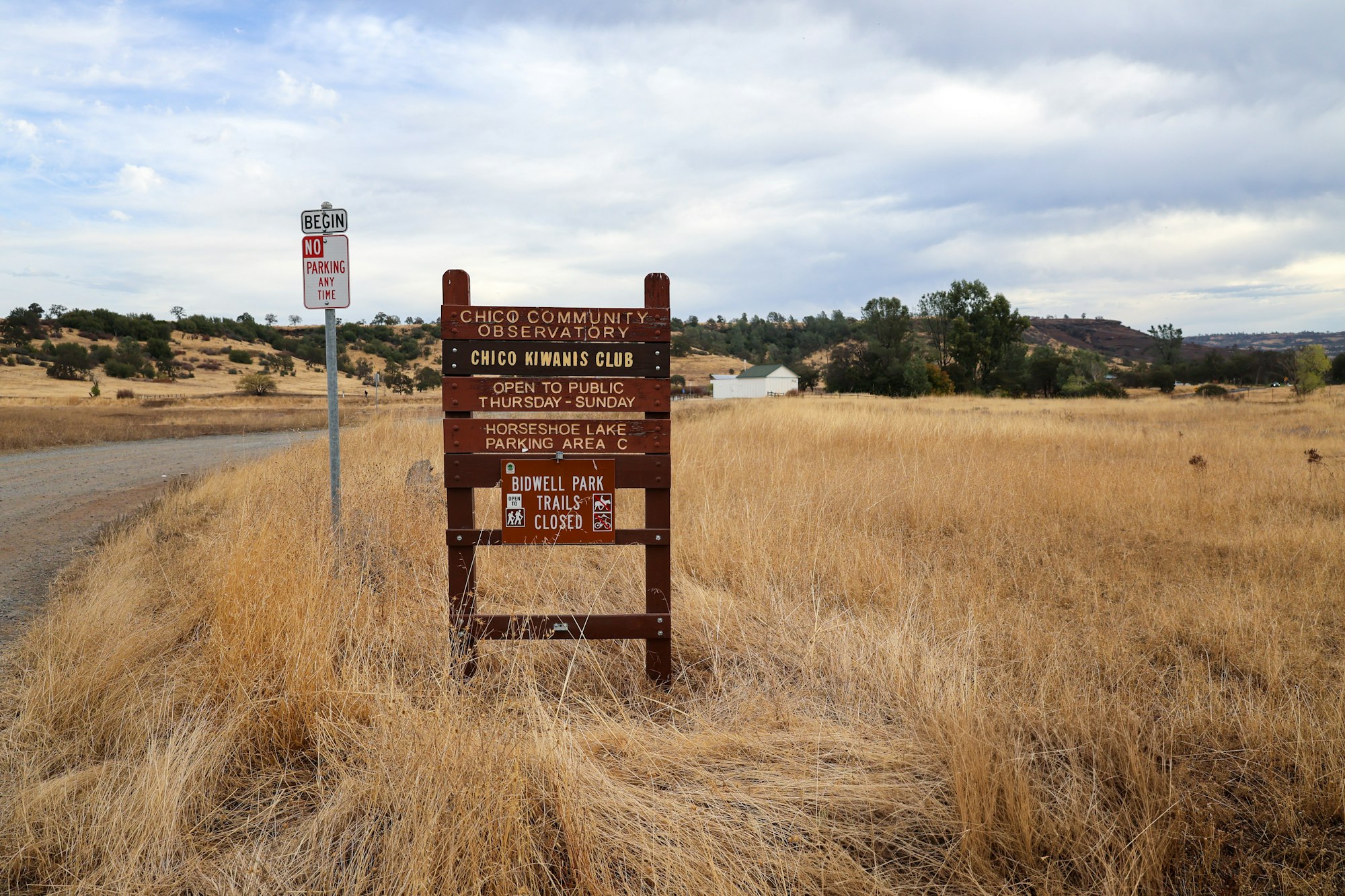 Rural landscape with signage for a community observatory and park. Dry grassland and cloudy sky.