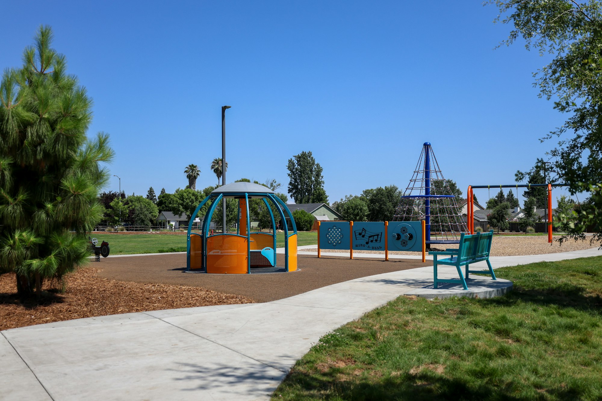 Playground with equipment, a bench, and trees under a clear blue sky.