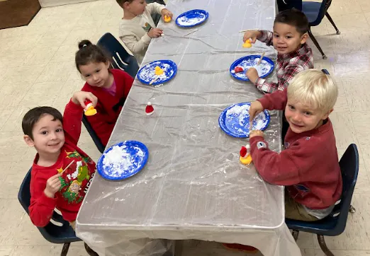 Children seated at a table are decorating items with colorful materials, having fun in a festive activity.