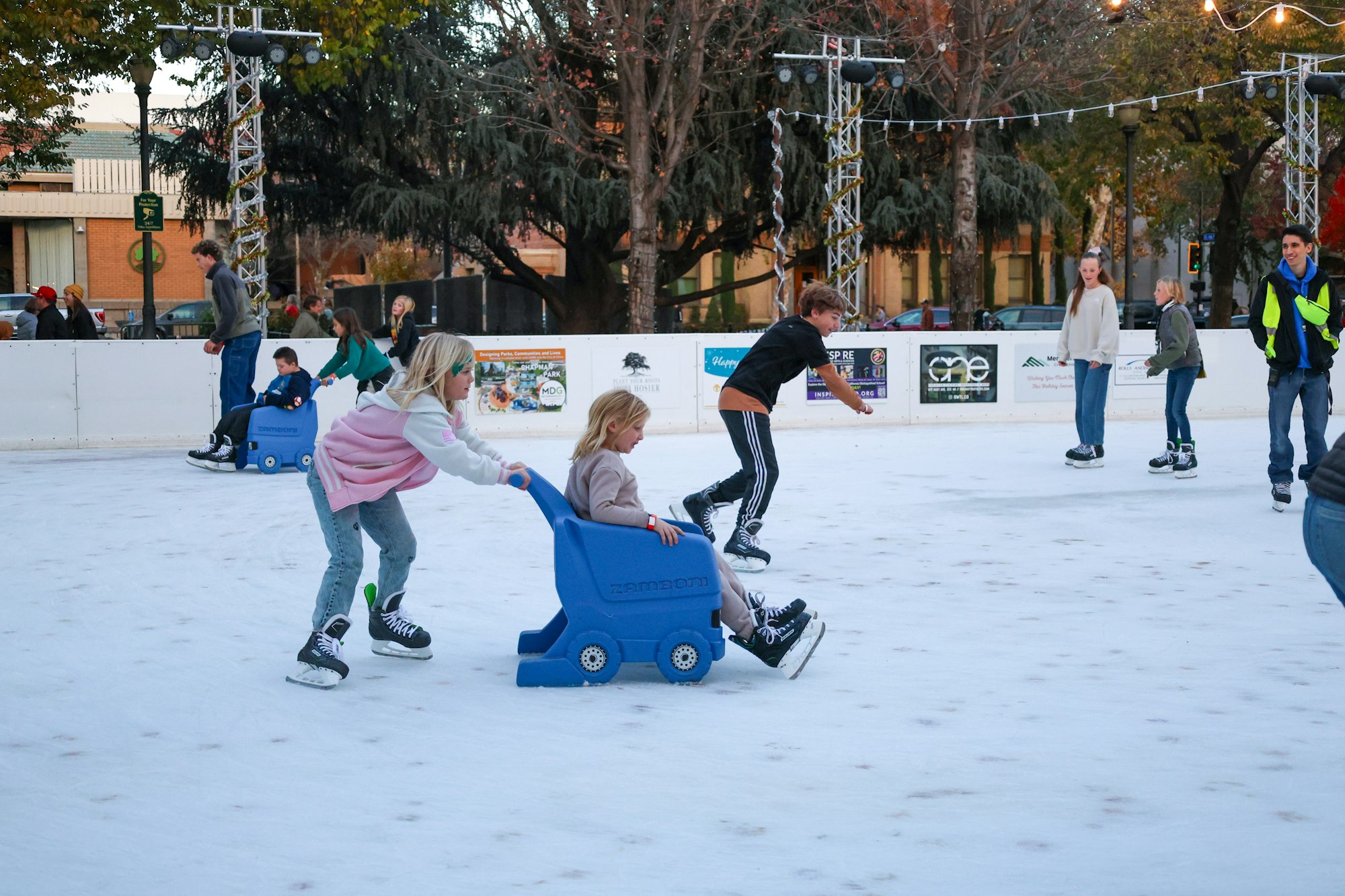 People ice skating, with some using sled pushers, on an outdoor rink.