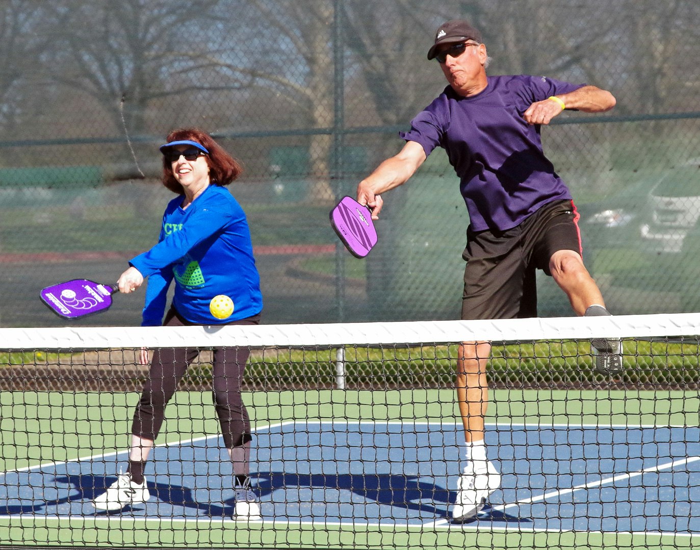 Two people are playing pickleball on a court, with one preparing to hit the ball while the other is in a ready position.