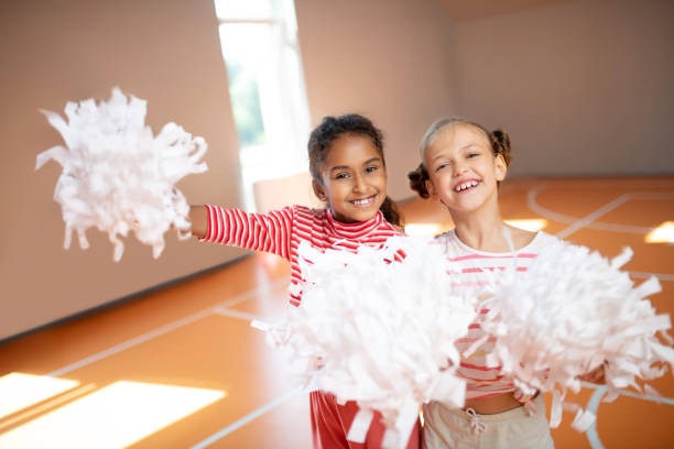 Two smiling children with pom-poms in a gym.
