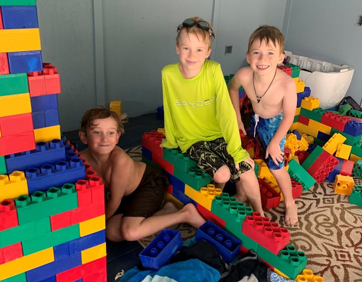 Three kids playing with large colorful interlocking building blocks indoors.