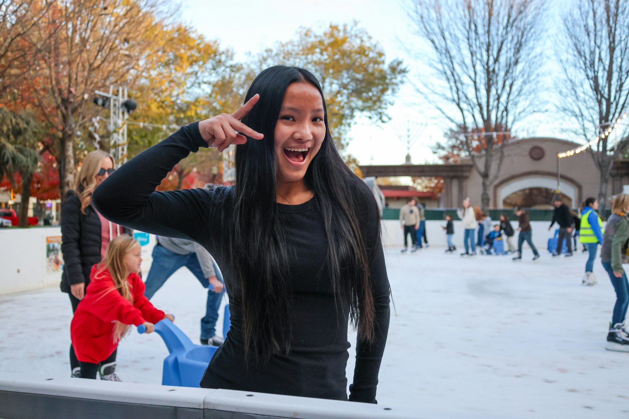 A person in black posing with a peace sign at an outdoor ice skating rink.