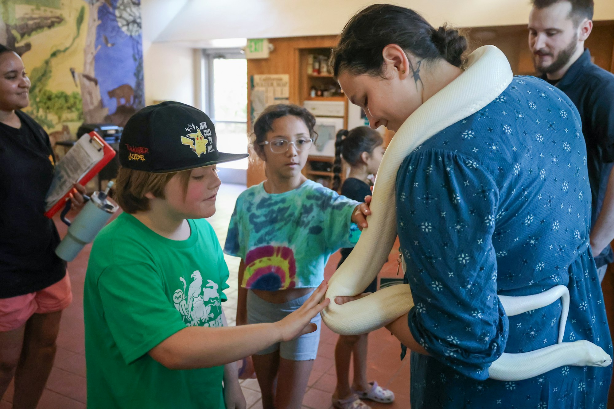 People interacting with a white snake, one holding it, others touching it, in an indoor setting.