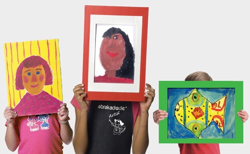 Three children are holding up colorful framed artworks: two portraits and one vibrant fish painting.