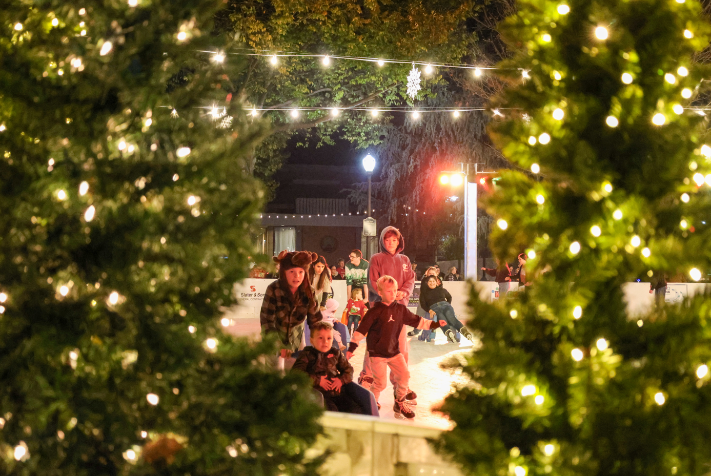 Children ice skating at night, surrounded by festive lights and decorations, creating a cheerful winter scene.