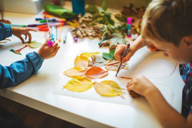 Children's hands, colorful autumn leaves, drawing supplies on a table, engaged in a crafting activity.