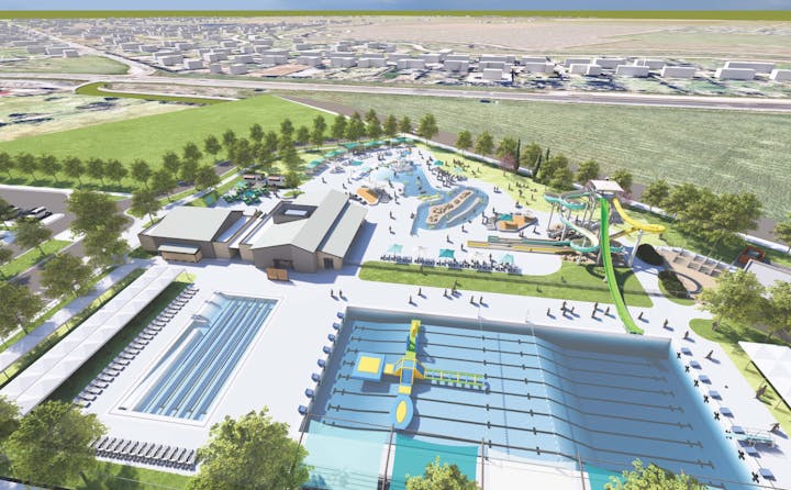 Aerial view of a waterpark with slides, pools, and buildings surrounded by green fields and a cityscape in the distance.