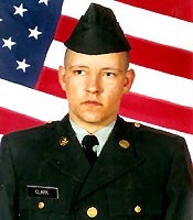 A person in military uniform stands before an American flag backdrop.