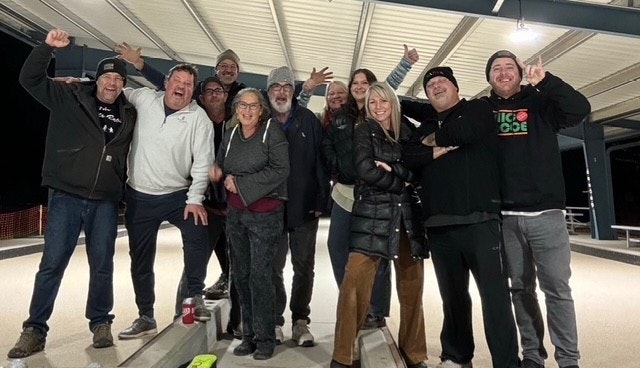 A group of people posing together in an outdoor covered area, smiling and making gestures, some wearing winter clothing.