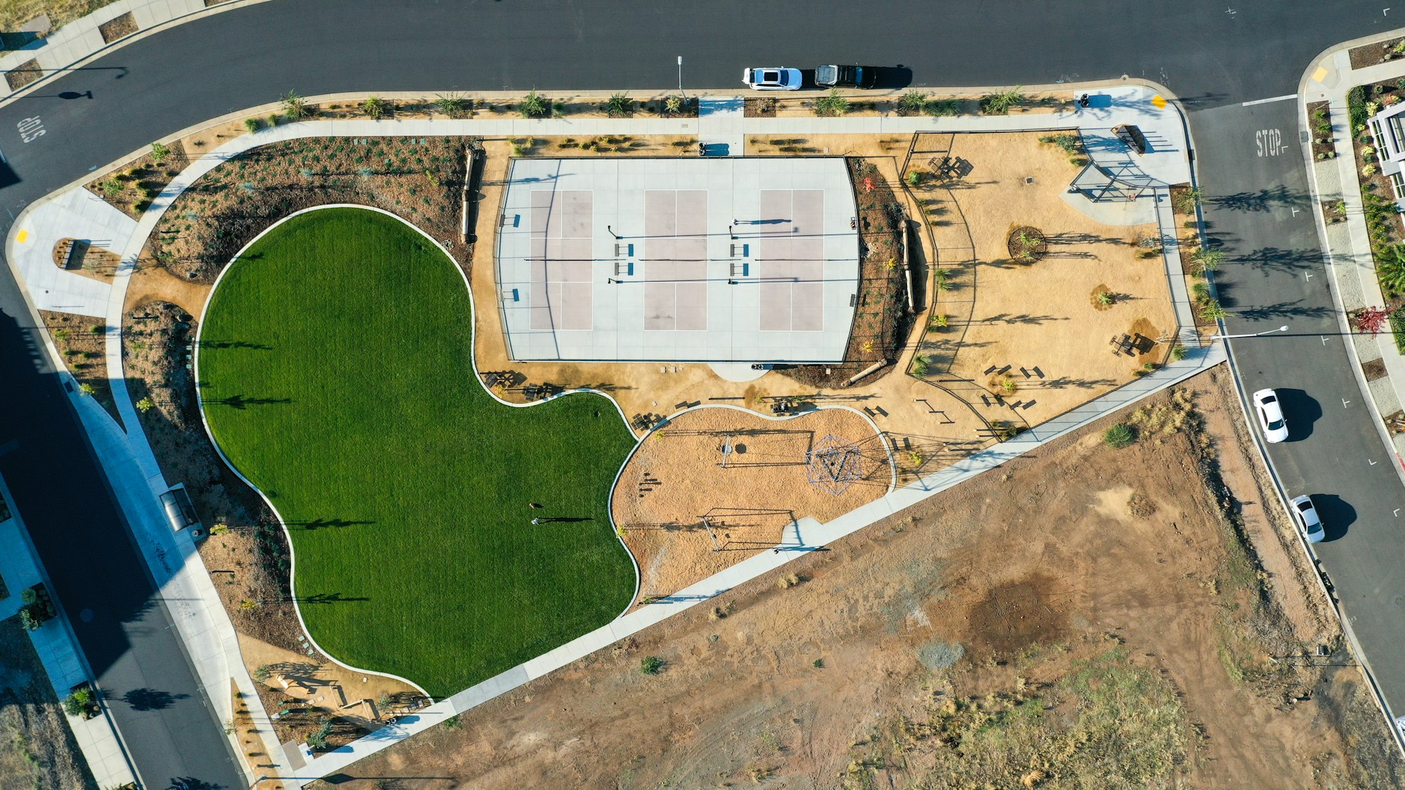 Aerial view of a park with a basketball court, playground, and grassy area surrounded by roads.